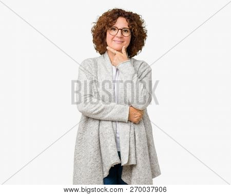 Beautiful middle ager senior woman wearing jacket and glasses over isolated background looking confident at the camera with smile with crossed arms and hand raised on chin. Thinking positive.
