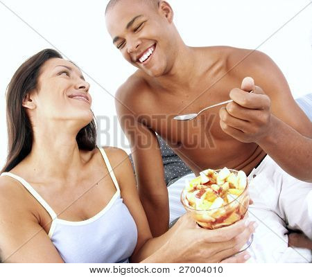 Unge hispanic par nyder og spise frugtsalat på sengen.