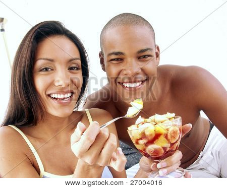 Unge hispanic par nyder og spise frugtsalat på sengen.