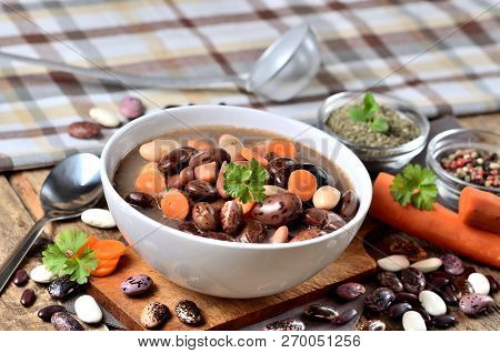Bowl Of Bean Soup With Large Beans On Cutting Board, Carrots, Parsley, Marjoram, Spoon, Towel And La