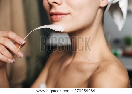 Close up pof pretty young woman wrapped in towel holding a feather indoors