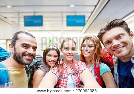 travel, tourism and people concept - group of smiling friends or tourists with backpacks taking selfie over airport terminal background