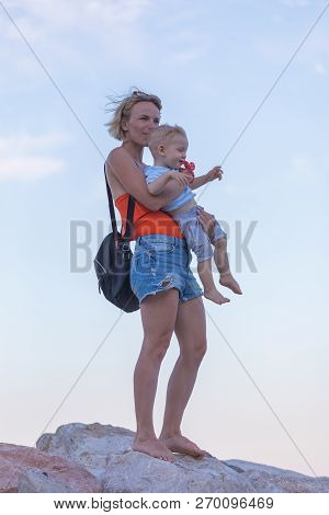 Woman Playing With Her Baby Outside Against The Sea. The Concept Of A Happy Full-fledged Family Life