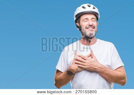 Middle age senior hoary cyclist man wearing bike safety helment isolated background smiling with hands on chest with closed eyes and grateful gesture on face. Health concept.