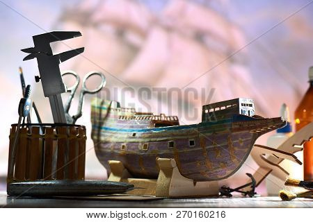 Model Of The Old Ship Frigate Made In Hands From The Cardboard. Near Glue, Brushes, Scissors And Sta