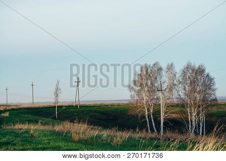 Atmospheric Landscape With Power Lines In Green Field With Road And Trees Under Blue Sky. Background