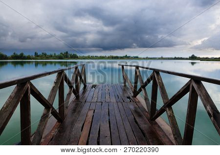Old Wooden Pier Bridge Leading To The Lake With Beautiful View And Skyscape At The Sunset.