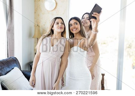 Smiling Young Bride And Bridesmaids Taking Selfportrait On Wedding Day In Living Room