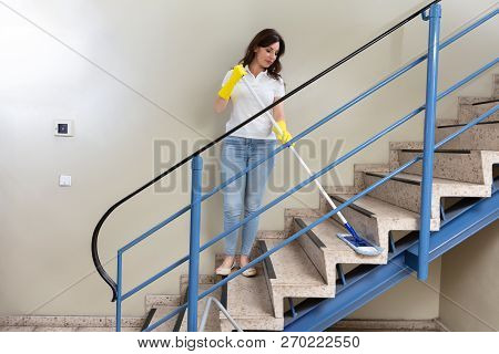 Young Female Janitor Cleaning Staircase With Mop