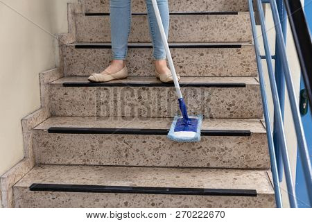 Young Female Janitor Cleaning Staircase With Mop
