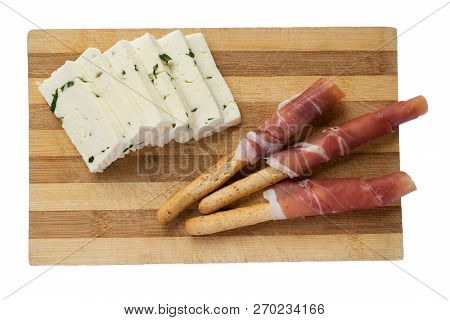 Cheese With Greens And Breadsticks With Prosciutto On A Wooden Board. Isolated On White Background.