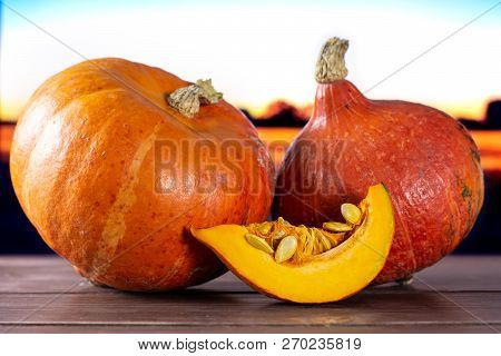 Group Of Two Whole One Slice Of Fresh Red Kuri Pumpkin Hokkaido Variety With Autumn Field And Sunset