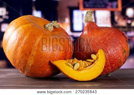 Group Of Two Whole One Slice Of Fresh Red Kuri Pumpkin Hokkaido Variety With Restaurant In Backgroun