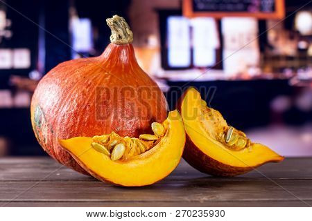 Group Of One Whole Two Slices Of Fresh Red Kuri Pumpkin Hokkaido Variety With Restaurant In Backgrou