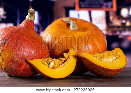 Group Of Two Whole Two Slices Of Fresh Red Kuri Pumpkin Hokkaido Variety With Restaurant In Backgrou