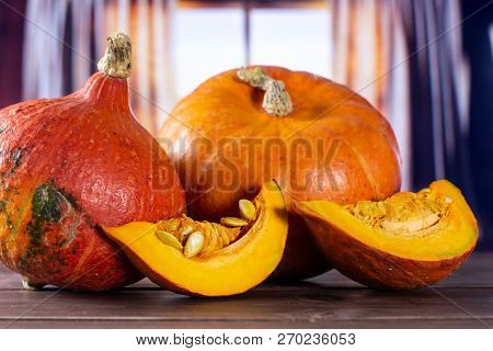 Group Of Two Whole Two Slices Of Fresh Red Kuri Pumpkin Hokkaido Variety With Silk Curtains Behind