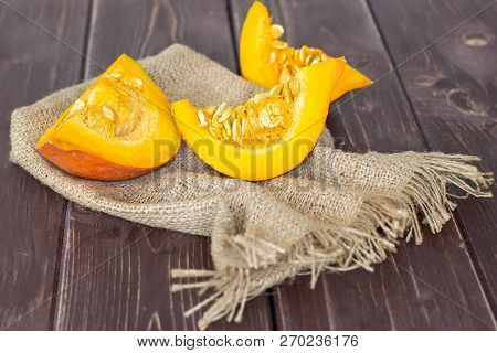 Group Of Three Slices Of Fresh Red Kuri Pumpkin Hokkaido Variety On Jute Cloth On Brown Wood