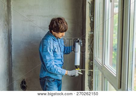 Man In A Blue Shirt Does Window Installation. Using A Mounting Foam