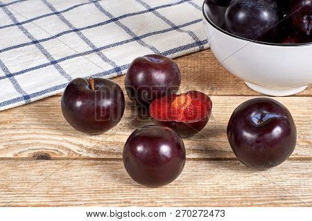 Opened Plum With A Ossicle Beside Several Plums, In Front Of Bowl With Red Plums And On Wooden Backg