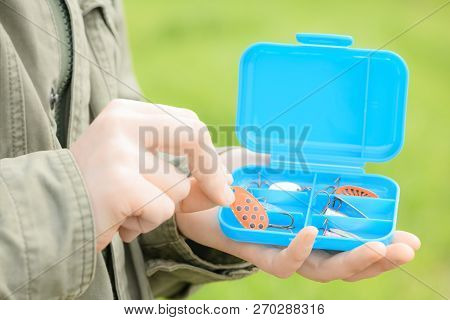 The Blue Plastic Container With Fishing Spoon Is In Woman's Hands On A Blurred Green Background. A F