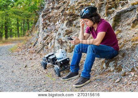 Young Caucasian  Man Sitting On Rock With Mountainboard And Cellphone In Nature