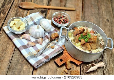 Garlic Soup In An Old Saucepan, Fresh Garlic Bulbs, Cloves, Colored Pepper, Wooden Spoon, Croutons A