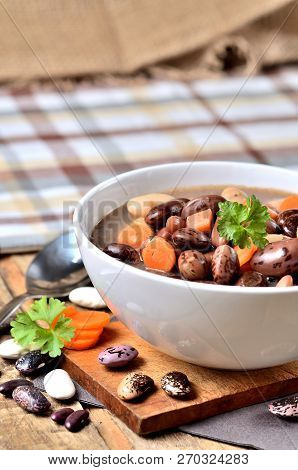 Bowl Of Bean Soup With Large Beans On Cutting Board, Carrots, Parsley, Marjoram, Spoon And Ladle, To