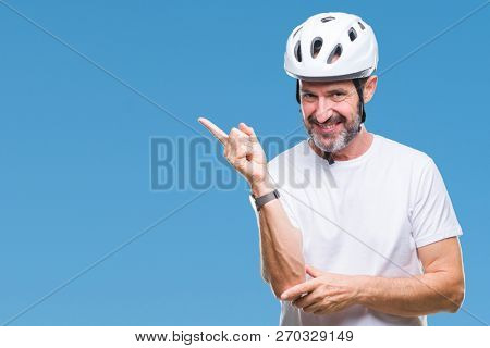 Middle age senior hoary cyclist man wearing bike safety helment isolated background with a big smile on face, pointing with hand and finger to the side looking at the camera.