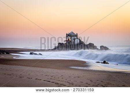 Side View Of Senhor Da Pedra Chapel At Sunset With Waves Crashing In The Sand. Golden Hour. Copy Spa