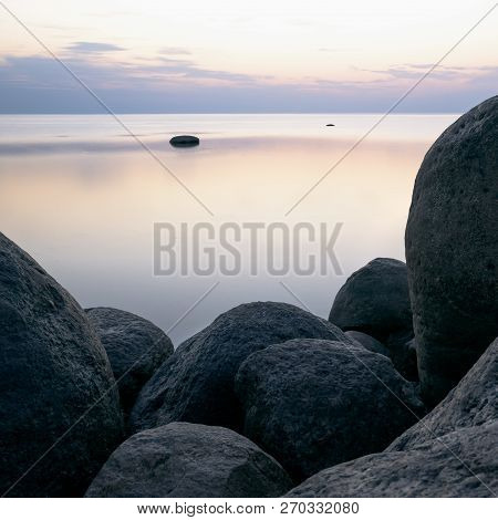 Large Stones On The Background Of The Sea At Sunset Tonted With Orange.