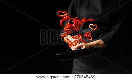 Professional Cook. Chef Preparing Dish With Red Sweet Pepper In A Pan, Paprika. On A Black Backgroun
