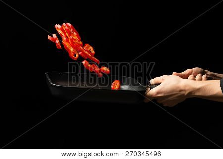 Professional Cook. Chef Preparing Dish With Red Sweet Pepper In A Pan, Paprika. On Black Background.