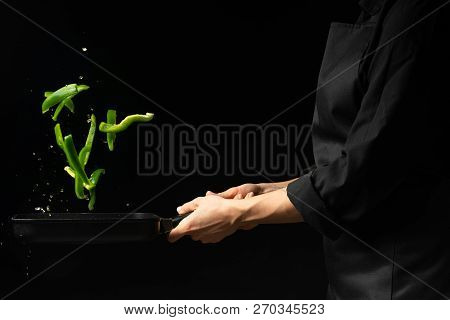 Professional Cook. He Prepares A Dish With Green Sweet Peppers In A Saucepan. On Black Background, M
