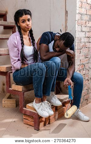 Young Afircan American Woman Cheering Up Tired Boyfriend With Paint Roller During Renovation Of Home