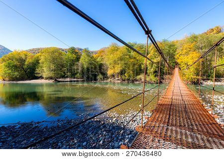 Narrow Metal Foot Bridge Across Mountain River In Autumn.