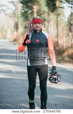 Training An Athlete On The Roller Skaters. Biathlon Ride On The Roller Skis With Ski Poles, In The H