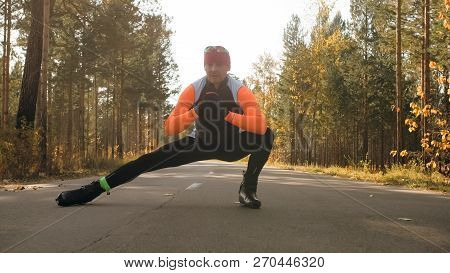 Training An Athlete On The Roller Skaters. Biathlon Ride On The Roller Skis With Ski Poles, In The H