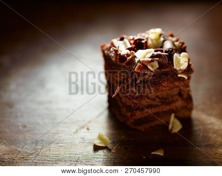 A Closeup Of A Cubed Piece Of Chocolate Case Over A Wooden Table. A Delicious Small Piece Of Chocola