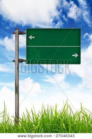 grüne Verkehrszeichen auf grünem Gras und blauen Himmel.
