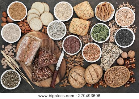 High fibre health food with whole grain bread and rolls, whole wheat pasta, grains, nuts, seeds, oatmeal, oats, crackers, barley and bran flakes on lokta paper background.