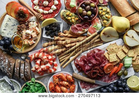 Italian antipasti snacks set. Brushettas, cheese variety, shrimps, salmon, olives, prosciutto with pear, salami and jamon over grey grunge table, top view. Food photography