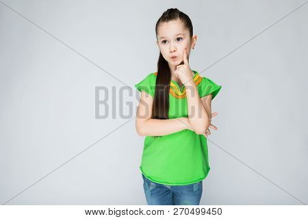 Girl On A Gray Background Put Her Finger To Her Cheek.