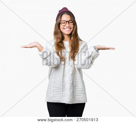 Young beautiful brunette hipster woman wearing glasses and winter hat over isolated background Smiling showing both hands open palms, presenting and advertising comparison and balance