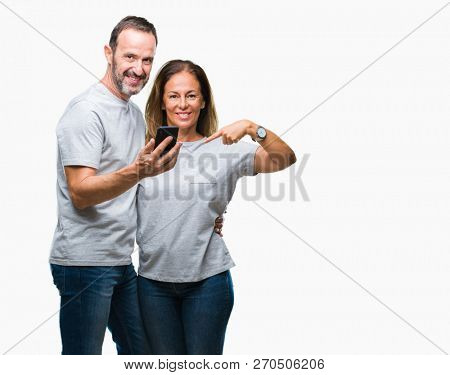 Middle age hispanic couple texting message on smartphone ver isolated background with surprise face pointing finger to himself