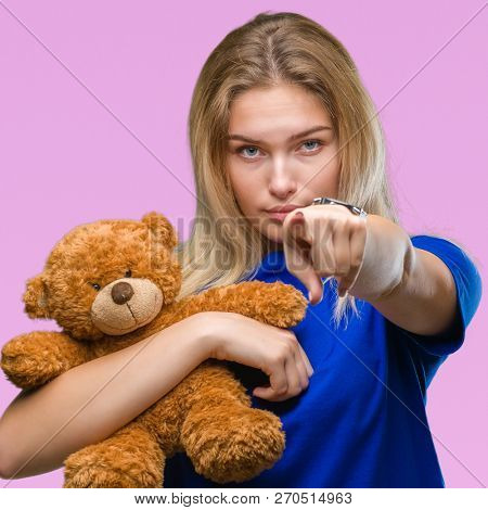 Young caucasian woman holding cute teddy bear over isolated background pointing with finger to the camera and to you, hand sign, positive and confident gesture from the front