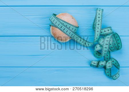Donut And Measuring Tape On Wooden Background. Doughnut Wrapped In Measuring Tape, Copy Space. Diet 