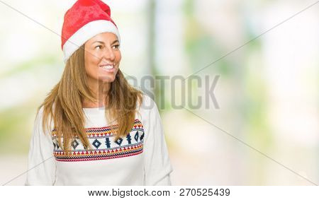 Middle age adult woman wearing winter sweater and chrismat hat over isolated background looking away to side with smile on face, natural expression. Laughing confident.