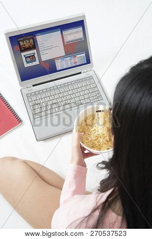 Girl Running Ebusiness On Notebook Computer While Eating Instant Noodle In Hurry Time On Bed.
