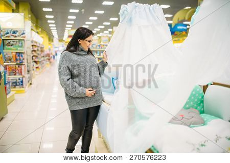 Pregnant woman choosing baby cot in store