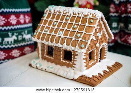 Homemade Christmas Gingerbread House In The Snow. Decorated Christmas Tree In The Background